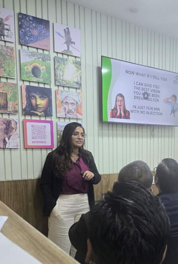 Dr. Devanshi Shah giving a patient talk at Deevine Eye Care beside her ArtByDrDee paintings
